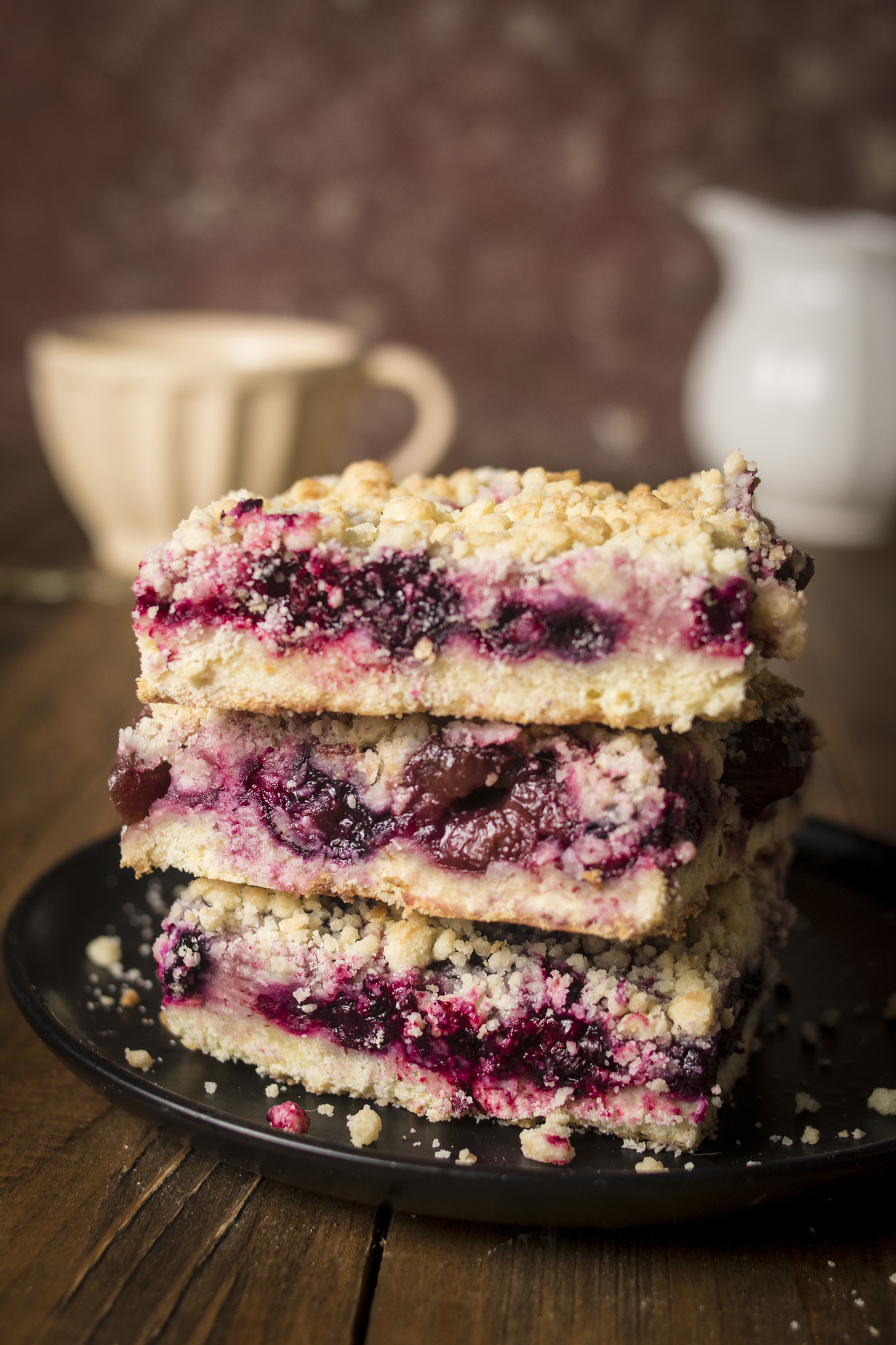 Stacked slices of sbriciolata ai frutti di bosco with golden crumble topping, vivid berry filling and a soft buttery base.
